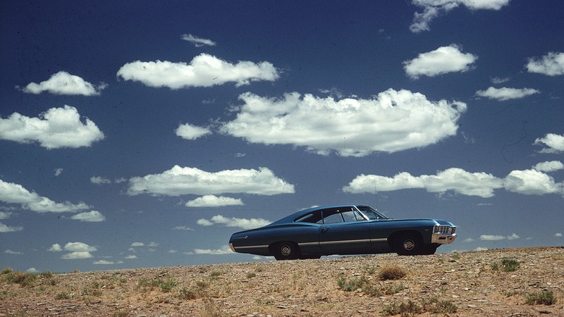 A blue car on the highway in the 70's.